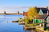 Holzhäuser und Windmühle spiegeln sich im blauen Wasser des Flusses Zaan Zaanse Schans Nordholland Niederlande Europa