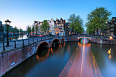 Dusk lights on the typical buildings and bridges reflected in a typical canal Amsterdam Holland The Netherlands Europe
