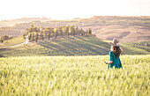 Ein Mädchen in einem grünen Kleid durch die goldenen Felder der Toskana, Val d'Orcia, Provinz Siena, Toskana, Italien