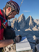 Sesto/Sexten, Dolomites, South Tyrol, province of Bolzano, Italy, Hiker sign the book of the summit of Monte Paterno/Paternkofel on the Tre Cime di Lavaredo/Drei Zinnen