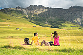 a couple of tourists is sitting on a meadow on the Seiser Alm, (Alpe di Siusi), Bolzano province, South Tyrol, Trentino Alto Adige, Italy