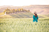 Ein Mädchen in einem grünen Kleid durch die goldenen Felder der Toskana, Val d'Orcia, Provinz Siena, Toskana, Italien