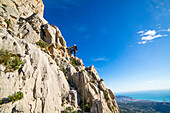 A man rock climbing high on the peak of Puig Campana above the city of Benidorm, Alicante Region, Costa Blanca in Mediterranean Spain.