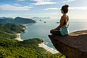 Frau sitzt am Rande des Berges in Pedra do Telégrafo, Barra de Guaratiba, Westseite von Rio de Janeiro, Brasilien