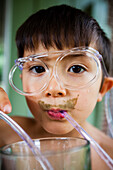A 6 year old Japanese American boy drinks greens from his weird straw glasses.