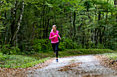 woman wearing a pink top and running alone on a road in a green forest in Autumn, close to Eloise, France