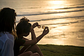 Zwei Frauen sitzen am Strand bei Sonnenuntergang