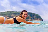 Portrait of young woman lying on surfboard in water