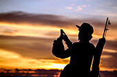 Silhouette of fisherman taking picture with smartphone at sunset