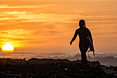 Silhouette der einsamen weiblichen Surfer zu Fuß in Richtung Ozean bei Sonnenuntergang, Elands Bay, Western Cape, Südafrika
