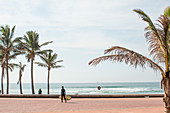 Ein Junge mit einem Surfbrett geht die Promenade entlang an der Goldenen Meile - benannt nach den goldenen Sandstränden - Durban, Südafrika.