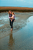 A woman walks near shallow water carrying her daughter in her arms in a marsh at Wrightsville Beach, North Carolina.