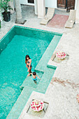 Erhöhte Ansicht der Mutter im Bikini mit Sohn in Badehose im Schwimmbad im marokkanischen Riad, Marrakesch, Marokko