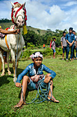 Boy sitting on grass and holding horse at Pasola Festival, Sumba island, Indonesia