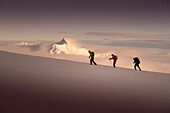 Three ski mountaineers ascending Denali, with sunset over Mount Hunter in the background. Denali National Park is a great location for backcountry skiing and mountain climbing tours.