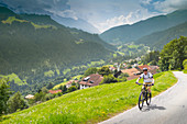 Mann Mountain Biken auf einem Schotterweg über eine Bergauf mit dem kleinen Dorf im Hintergrund