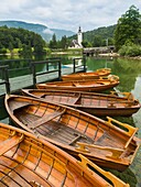 Lake Bohinj (Bohinjsko jezero), Triglav National Park, Upper Carniola, Slovenia. Rowing boats for rent. The church of St. John (Cerkev sv Janeza) at Ribcev Laz in background.