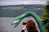 Frau fotografiert Nessi-Model am Loch Ness Westufer, Highlands, Schottland