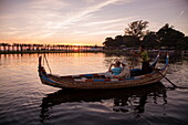 Touristen auf Ruderboot mit Silhouette von Menschen die auf der U-Bein-Brücke über den Taungthaman See laufen bei Sonnenuntergang, Amarapura, Mandalay, Myanmar