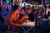Junges Paar genießt Cocktails und frische Kokosnuss im The Green Umbrella Beach Restaurant und Bar am Strand Ngapali Beach