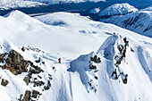 Die professionellen Snowboarder Marie France Roy, Robin Van Gyn und Helen Schettini stehen auf einem Berg und bereiten sich auf ihre Snowboards vor, nachdem sie an einem sonnigen Tag in Haines, Alaska, von einem Hubschrauber abgesetzt wurden.
