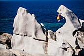 Bemannen Sie das Klettern auf Felsen nahe Meer, Capo Testa, Sardinien, Italien