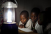 A group of boys read their homework by the light of a solar lantern, Tanzania, East Africa, Africa
