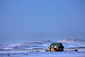 Winterlandschaft in der Abenddämmerung zeigt einsame Kabine im Abendsonnenlicht, in der Nähe von Seljalandsfoss, Südisland, Polargebiete gebadet