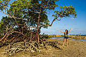 Fotografie der jungen Frau mit den offenen Armen, die nahe Mangrovenbäumen auf tropischem Strand, Morro de Sao Paulo, Bahia, Brasilien stehen