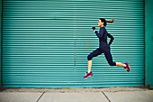 Weiblicher Rüttler, der gegen grüne Wand, Boston, Massachusetts, USA läuft und springt.