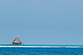 Thatched roof huts sit above the ocean off an island in the area of Glover's Reef, Belize.