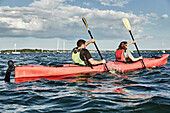 Couple using teamwork while paddling in tandem sea kayak, Portland, Maine, USA
