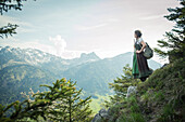 Young woman in traditional costume enjoying the view to the Aggenstein on the Falkenstein, Pfronten, Bavaria, Germany