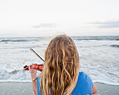 Rear view of Caucasian girl playing violin at beach