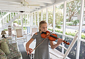 Caucasian girl playing violin on patio
