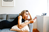 Mixed race woman laying on sofa texting on cell phone