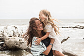 Caucasian mother hugging daughter near driftwood on beach