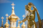 Detail of golden statue at Grand Cascade fountains at Peterhof Palace (Petrodvorets) with golden spires of church behind, St. Petersburg, Russia