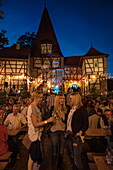 Three young women enjoy Frankenwein Franconian wine at Weinfest am Rödelseer Tor wine festival at dusk, Iphofen, Franconia, Bavaria, Germany