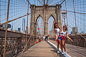 young tourists on the brooklyn bridge taking selfies with their cell phones and a selfie stick with one world trade center in the background, brooklyn bridge, manhattan, new york city, state of new york, united states, usa