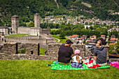 family having a picnic on the lawn of montebello castle across from castelgrande castle, listed as a world heritage site by unesco, bellinzona, canton of ticino, switzerland