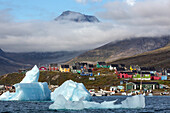 icebergs that separated from the glacier snouts in the fjord in front of the colorful wooden houses of the village of narsaq, greenland