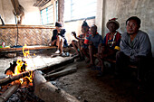 Naga men sitting chatting round fire in village muting (meeting hall), Nagaland, India, Asia