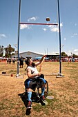 A kilted young man in a wheelchair competes in the 'Sheaf Toss' at a Scottish festival in Costa Mesa, CA, using a pitchfork to toss a 16-pound burlap bag of straw over a bar
