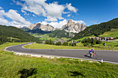 View toward Corvara and road cyclist, Alta Badia, Corvara, Dolomites, South Tyrol, Italy, Europe