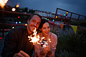 Happy couple holding sparklers on patio at night