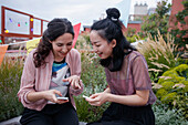 Happy female friends using smart phones while sitting on patio