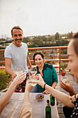 Happy friends toasting wineglasses at outdoor table on patio