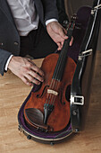 Midsection of man keeping violin in case at table