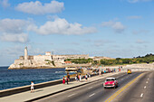 red oldtimer, driving along Malecon, in the backround Castillo De Los Tres Reyes Del Morro, historic town, center, old town, Habana Vieja, Habana Centro, family travel to Cuba, holiday, time-out, adventure, Havana, Cuba, Caribbean island
